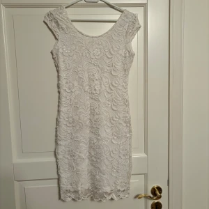 Vit spetsklänning - Säljer en så fin vit spetsklänning med blommiga detaljer. Klänningen har en figurnära passform som VERKLIGEN framhäver midja och höfter!! Den är ärmlös men har går ner kort över axlarna. Halsen är rundad och ryggen är lagom djup för att ge en extra detalj men ändå täcka bh i bak. Längden är lår- knälång. Storlek S men funkar även som XS och som M (om man vill ha den tight och kort). Aldrig använd.
