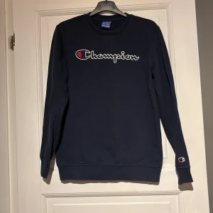 Mörkblå sweatshirt från Champion - Säljer en mörkblå sweatshirt från Champion med deras ikoniska logga på bröstet. Tröjan har långa ärmar och en rund halsringning. Perfekt för en avslappnad stil.