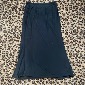 Svart långkjol - Elegant svart långkjol i ett mjukt och följsamt material. Perfekt för en stilren look. Kjolen har en enkel design utan detaljer och passar till många olika tillfällen.