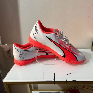 Fotbollsskor och sneakers i olika storlekar - Säljer ett par vita och röda fotbollsskor med snörning och ett par beige sneakers med blå och gula detaljer. Fotbollsskorna har en sportig design med svarta accenter, medan sneakersen har en klassisk look med mocka och textilmaterial.