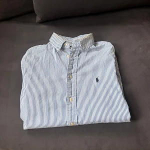 Randig skjorta från Ralph Lauren - Säljer nu denna vit-blå randiga Ralph Lauren skjortan som är helt perfekt för sommaren och våren, storlek S/18 och är i perfekt skick nypris är runt 1700, inga defekter, hör gärna av er vid frågor.