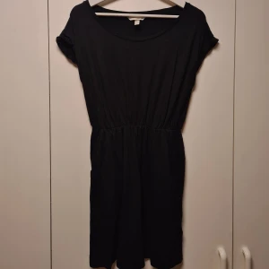 Svart klänning från H&M - Säljer en enkel och stilren svart klänning från H&M. Klänningen har korta ärmar och en elastisk midja som ger en bekväm passform. Perfekt för en avslappnad look. Klänningen är lite nopprig men det känns eller syns inte förens man tittar nära.