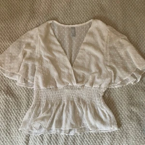 Vit blus från Amisu - Säljer en söt vit blus från Amisu med v-ringning och smockdetaljer i midjan. Kan passa strl M och L (köparen står för frakten!)