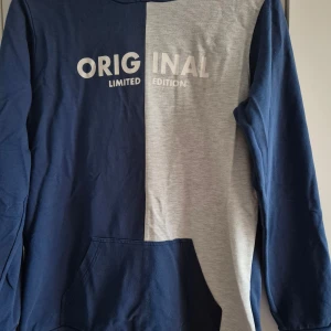 Blå och grå hoodie med text - Säljer en cool hoodie i tvåfärgad design, blå och grå, med texten 'ORIGINAL LIMITED EDITION' på framsidan. Tröjan har en praktisk magficka och långa ärmar. Perfekt för en avslappnad stil.