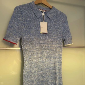 Blå klänning från Tommy Hilfiger - Snygg blå klänning från Tommy Hilfiger med korta ärmar och krage. Klänningen har en fin textur och detaljer i rött och vitt vid ärmsluten. Perfekt för en stilren look! Klänningen är oanvänd och med alla etiketter på. 