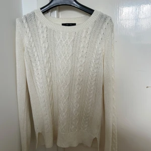 Vit stickad tröja från Lindex - Säljer en stilren vit stickad tröja från Lindex i storlek XS. Säljer på grund av att jag fick den i present men den var för stor. Tröjan har ett klassiskt flätmönster och långa ärmar, perfekt för kyligare dagar. Den är mjuk och bekväm, idealisk för både vardag och mysiga stunder hemma.
