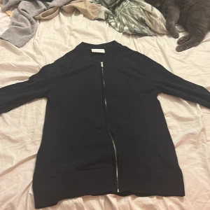 Svart långärmad tröja med dragkedja - Säljer en stilren svart jacka med dragkedja framtill. Jackan har långa ärmar och en enkel design som passar perfekt för en avslappnad look. Perfekt för svala dagar!