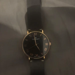 Svart klocka med romerska siffror - Elegant klocka från Frederic Graff med svart urtavla och guldiga romerska siffror. Klockan har en tunn boett i guld och ett svart läderarmband. Perfekt för en stilren look. Nypris 2500kr men varför jag säljer den så billigt är för att batteriet är dött. Så måste bara byta batteri sen så gör den som en klocka. Kontakta mig för frågor😃