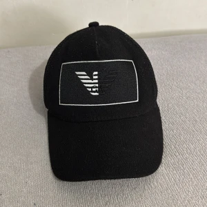 Svart keps med broderad logga - Snygg svart keps med broderad logga framtill. Kepsen har en klassisk design med böjd skärm och mesh-paneler på sidorna för bättre ventilation. Perfekt för en stilren look.