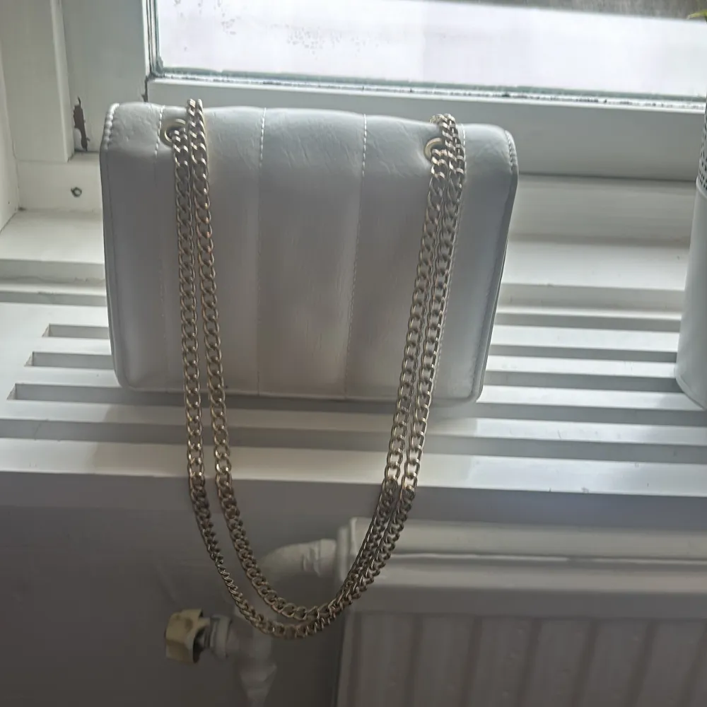 Snygg vit axelväska med quiltad design och guldfärgad kedja. Perfekt för att ge en stilren touch till din outfit. Väskan har en elegant och kompakt form, vilket gör den lätt att bära med sig.🩷. Laukut & Käsilaukut.