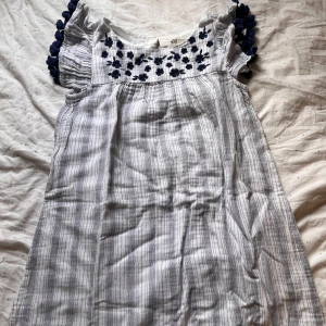 Randig klänning från H&M - Söt randig klänning från H&M med blå broderade detaljer på bröstet och volangärmar med mörkblå bollar. Perfekt för en somrig dag! 💙