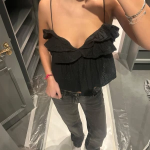 Svart ärmlös topp från Zara - Säljer en snygg svart ärmlös topp från Zara med volangdetaljer och smala axelband. Toppen har en öppen rygg med knytning och är perfekt för en stilren look.