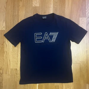 Emporio Armani T-shirt - Snygg mörkblå t-shirt från Emporio Armani med logga på bröstet. I bra skick – inga skador eller fläckar. Tillverkad av 100 % bomull.