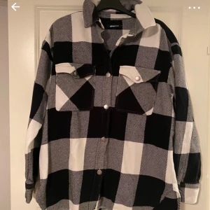 Svartvit rutig overshirt från Gina Tricot - Säljer en snygg svartvit rutig overshirt från Gina Tricot. Den har långa ärmar och knappar framtill samt två stora bröstfickor. Perfekt för lager-på-lager-stilen!