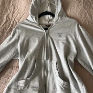 Grå hoodie från Playboy - Säljer min Gråa zip hoodie från Playboy med Playboy loggan på bröstet, jätte fint skick! Storlek L men passar M och S också 