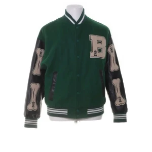 Grön bomberjacka från Aelfric Eden - Snygg grön bomberjacka från Aelfric Eden med svarta ärmar och coola benmotiv. Jackan har en stor broderad bokstav 'B' på bröstet och ribbade muddar. Perfekt för en unik stil!