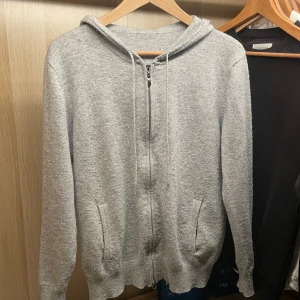 Grå merinoull hoodie - Säljer en stilren grå merinoull hoodie med dragkedja och huva. Tröjan har långa ärmar och ribbade muddar vid ärmslut och nederkant. Perfekt för vardaglig användning och för att klä upp sig! Dessa är otroligt sköna och passar dig med XS-S perfekt! Lite luddig vilket lätt går att fixa med en ullkamm som kostar 49kr!