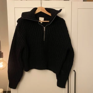 Svart stickad tröja med dragkedja - Säljer en svart stickad tröja med dragkedja och hög krage. Tröjan har en oversized passform och långa ärmar.