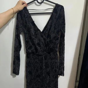 Svart glittrig klänning - Snygg svart klänning med glittrigt mönster och djup v-ringad design som går att anpassa. Den har långa ärmar och går lite över knäna samt en figurnära passform som ger en fancy look. Perfekt för en utekväll med vännerna eller ett speciellt tillfälle. Priset går att förhandlas💗