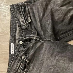 Svarta jeansbyxor från Zara - Snygga svarta baggy  jeansbyxor från Zara med dragkedja och knapp framtill. De har en klassisk design med fem fickor och en bekväm passform. Perfekta för en stilren look.