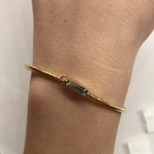 Guldarmband och örhängen med kristall - Elegant set med ett guldarmband och matchande örhängen, båda med en rektangulär kristalldetalj. Perfekt för att ge en touch av glamour till din stil. Armbandet har en enkel och stilren design som kompletteras av de subtila örhängena.