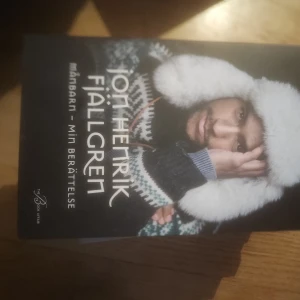 Månbarn - Min berättelse - Boken 'Månbarn - Min berättelse' av Jon Henrik Fjällgren är en personlig och gripande skildring av hans liv och erfarenheter. Omslaget visar en bild av författaren klädd i en varm, stickad tröja och en pälsmössa, vilket ger en känsla av närhet till naturen och hans samiska rötter.