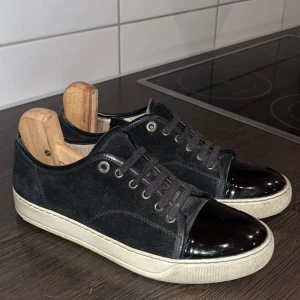 Lanvin skor - Snygga svarta sneakers i mocka med glansiga lackdetaljer på tån. Skorna har en vit sula och snörning framtill. Perfekta för en stilren look.