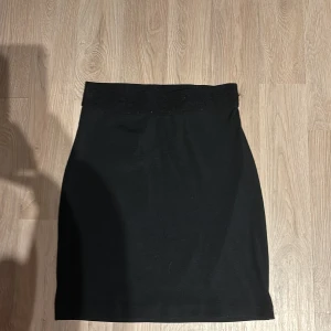 Svart kjol - Snygg svart kjol i klassisk stil. Perfekt för både vardag och fest. Den har en enkel design utan mönster eller detaljer, vilket gör den lätt att matcha med olika toppar och accessoarer. Ett måste i garderoben för alla tillfällen!