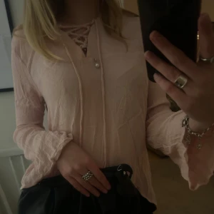 Ljusrosa blus med snörning - Säljer en söt ljusrosa blus med snörning framtill. Blusen har långa ärmar med volangdetaljer vid ärmsluten. Perfekt för vår och sommar! 💗
