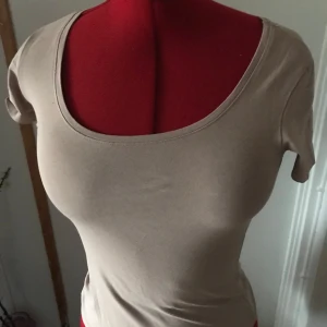 Beige topp från Amisu - Säljer en stilren beige topp från Amisu i storlek S. Den är kortärmad och har en rund halsringning. Perfekt för både vardag och festliga tillfällen. Materialet känns mjukt och bekvämt mot huden.