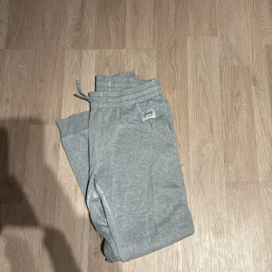 Grå mjukisbyxor från Frank Dandy - Säljer ett par grå mjukisbyxor från Frank Dandy i bra skick. De har en bekväm passform med resår i midjan och snörning för justering. Perfekta för en avslappnad dag hemma eller en snabb tur till affären. 