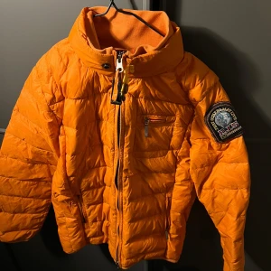 Orange dunjacka från Ape & Partners - Säljer en superlätt orange dunjacka från Ape & Partners. Jackan har en dragkedja framtill och en cool patch på ärmen. Perfekt för höst och vinter, håller dig varm och stilren. Passar bra till både vardag och utomhusaktiviteter. 🧡för barn 