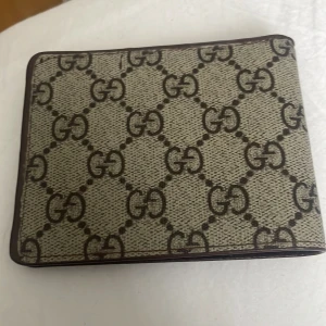 Plånbok med GG-mönster - Säljer en stilren plånbok med det klassiska GG-mönstret. Den är i en beige och brun färgkombination och har flera fack för kort och sedlar. Perfekt för dig som vill ha en snygg och praktisk accessoar. Tillverkad i Italien.