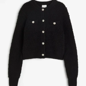 Svart kofta med knappar - Säljer en supermysig svart kofta med fluffig textur och snygga knappar framtill. Perfekt för kyliga dagar och att ha över en t-shirt eller blus. Koftan har långa ärmar och en klassisk rund halsringning. Passar både till vardags och lite finare tillfällen🥰😚🙌🏼💖 SLUTSÅLD!!