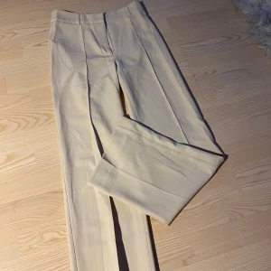 Beige kostymbyxor från Madlady - Säljer ett par stilrena beige kostymbyxor från Madlady i storlek EU 34 L30. Byxorna har en hög midja och raka ben. De är i mycket bra skick. Stretchigt material.