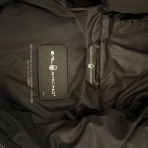 Svart blå jacka från Sail Racing - Säljer en svart jacka från Sail Racing i mycket bra skick. Jackan har en stilren design med dragkedja och huva. Perfekt för höst och vinter, tillverkad i slitstarkt material som håller dig varm. Passar både till vardags och utomhusaktiviteter.