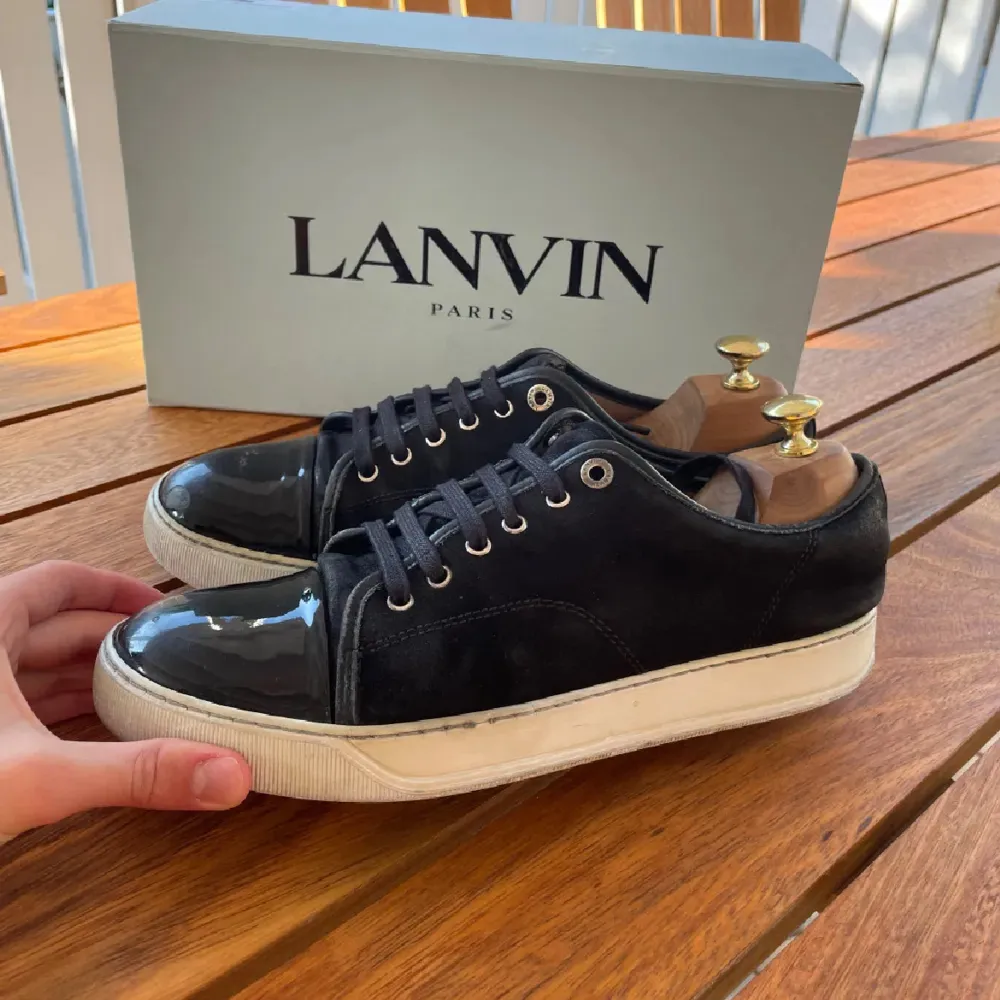 Säljer ett par snygga svarta sneakers från Lanvin. De har en glansig tå och snörning framtill. Skorna är i bra skick med lite slitage på sulorna 6/10. Perfekta för både vardag och fest!. Skor.