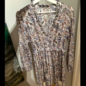 Mönstrad klänning från Zara - Säljer en superfin mönstrad klänning från Zara. Den har långa ärmar och resår i midjan samt armarna. Klänningen har en v-ringad hals och volangdetaljer. Kanske använt 2/3 gånger. Storlek s men funkar som en m också!