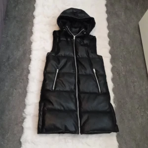 Svart dunväst med huva - Säljer en snygg svart dunväst med dragkedja och huva. Perfekt för höst och vinter. Västen är i nyskick. 