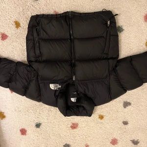 Svart dunjacka från The North Face - Säljer en svart dunjacka från The North Face i storlek XL i barn strl. Jackan är i mycket bra skick och perfekt för kalla vinterdagar. Den har en dragkedja framtill och är långärmad med elastiska ärmslut för extra värme. Fyllningen är 700-fill, vilket gör den supervarm och mysig. Perfekt för vintern!  Passade perfekt till mig när jag var cirka 170 lång! 