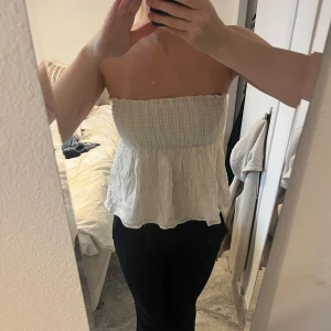 Vit axelbandslös topp med guldglitter - Säljer en superfin vit axelbandslös topp med guldglittriga detaljer. Den har en smockad överdel och en luftig passform nedtill. Toppen är i mycket bra skick och använd fåtal gånger. Köpt från barnavdelningen på Gina men sitter som en XS/S.