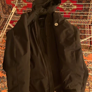 Svart jacka- Sail Racing- XL - Säljer en svart jacka med huva i mycket bra skick. Den har en quiltad insida för extra värme och en dragkedja framtill. Perfekt för höst och vinter. Jackan är stilren och passar till det mesta. Hör av dig om du är intresserad! 