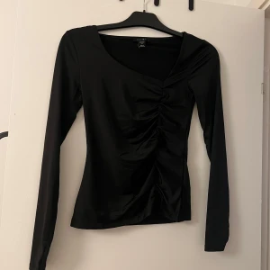 Svart långärmad topp från Amisu - Säljer en elegant svart långärmad topp från Amisu i storlek S. Toppen har en snygg rynkad detalj framtill som ger en smickrande passform. Perfekt för både vardag och fest! 🖤Tröjan är helt ny och aldrig använd! Nyskick! 