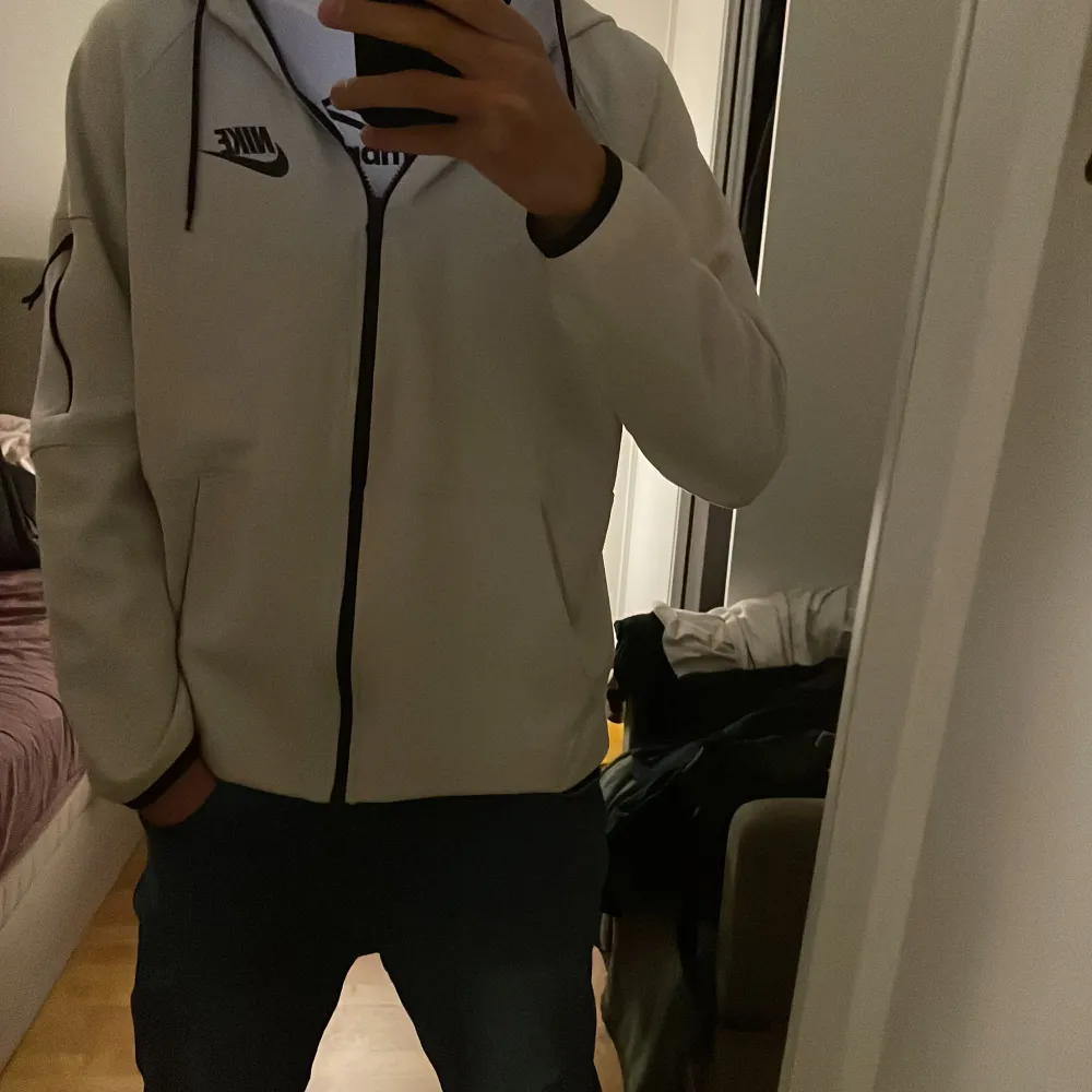 Säljer en vit hoodie från Nike i bra skick. Den har en dragkedja framtill och en justerbar huva med svarta snören. Perfekt för både vardag och träning. Det finns en liten fläck på framsidan, men annars är den i fint skick. Jag är 183cm och pris kan sänkas. Tröjor & Koftor.