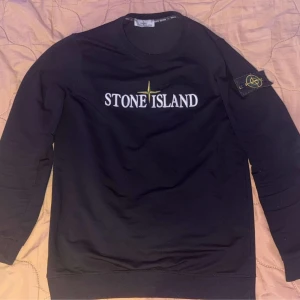 Svart tröja från Stone Island - Säljer en svart tröja från Stone Island i mycket bra skick. Den har en klassisk design med Stone Island-loggan på bröstet och en patch på ärmen. Perfekt för både vardag och fest!