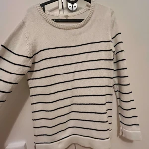 Vit och svart randig tröja - Säljer en stilren vit tröja med svarta ränder. Den är långärmad och perfekt för både vår och höst. Tröjan är i bra skick och passar till många olika outfits. Perfekt för en casual look!