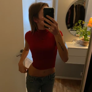 Röd croppad topp - Säljer en snygg röd croppad topp i tight passform. Perfekt för sommardagar eller en utekväll. Toppen är ärmlös och har en hög halsringning som ger en stilren look. Passar bra till jeans eller kjol för en trendig outfit.