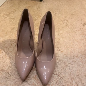 Beige pumps med klack - Snygga beige pumps i syntetmaterial med spetsig tå och hög klack. Perfekta för festliga tillfällen eller en elegant vardagslook. De är i mycket bra skick och har en stilren design som passar till det mesta.