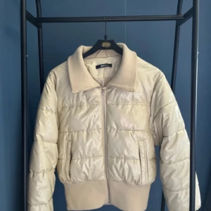 Beige pufferjacka från Gina Tricot - Säljer en snygg beige pufferjacka från Gina Tricot. Jackan har en dragkedja framtill och en ribbad krage som ger en cool look. Perfekt för höst och vinter, håller dig varm och stilren. Den är i mycket bra skick och passar perfekt till vardags eller en utekväll.