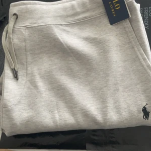Grå mjukisbyxor från Polo Ralph Lauren - Säljer ett par snygga grå mjukisbyxor från Polo Ralph Lauren. De är i nytt skick och har en klassisk design med snörning i midjan och det ikoniska logotypbroderiet på benet. Perfekta för en avslappnad stil eller mysiga dagar hemma. Prislapparna och alla taggar följer med varan . Pris kan diskuteras vid intresse. Frakt kan markeras som gratis beroende på priset när byxorna sålts. 
